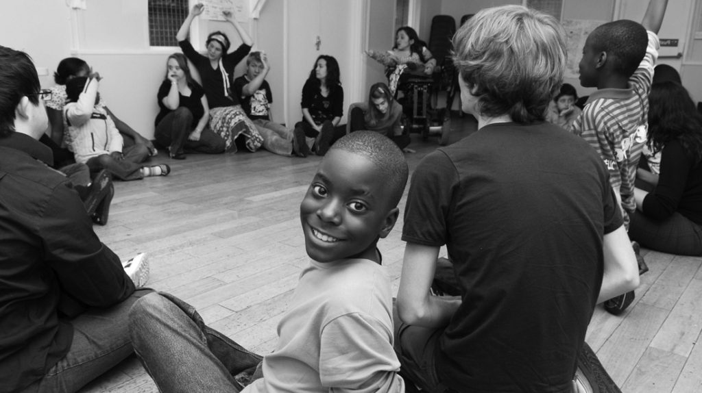 Boy smiling, sitting on floor in a circle.