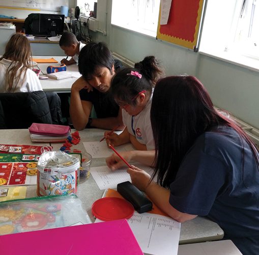 Teacher, child and teaching assistant in classroom sitting together looking at work