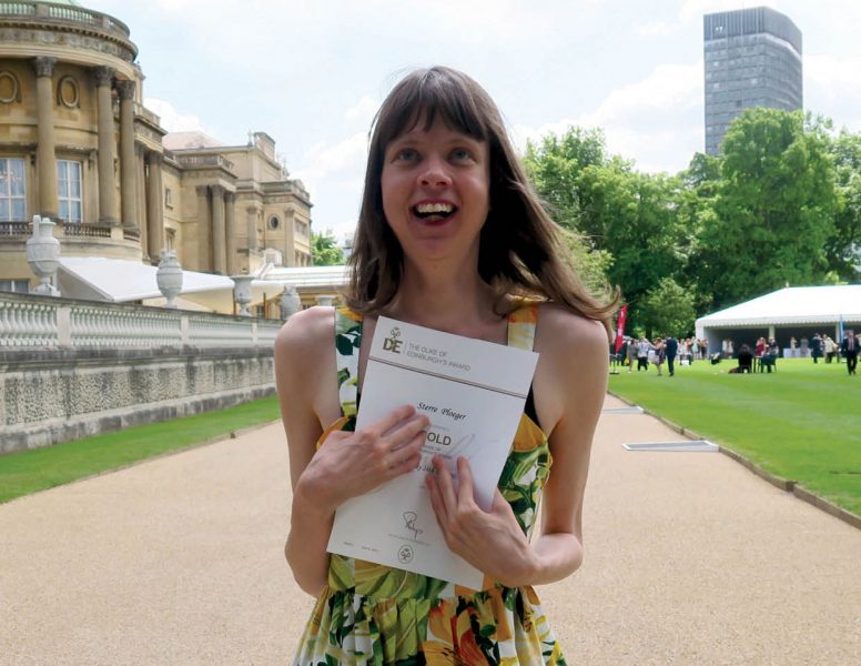 cover of Inclusion Now 48: a young disabled woman clutches her Duke of Edinburgh award certificate outside Buckingham Palace and smiles towards the sky