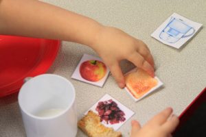 Child's hand with some cards with pictures of food on, and some actual food