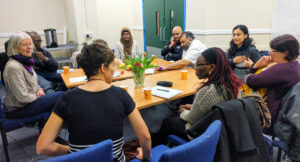 Ten people round a table talking in a workshop