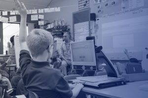 Young boy with his hand up in class