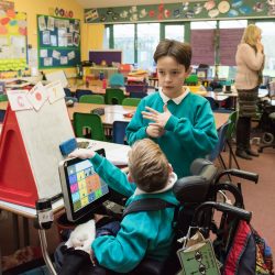 Two boys talking in a classroom, one in a wheelchair, one standing