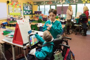 Two boys talking in a classroom, one in a wheelchair, one standing