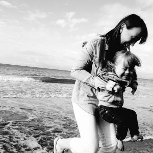 Leslie holding Ava on the beach, both laughing