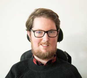 Miro Griffiths, smiling, using a wheelchair headrest