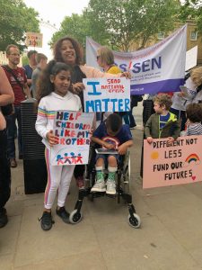 Woman, girl and boy (wheelchair user) - daughter holds placard saying "help children like my brother". Mother holds placard saying "I matter"