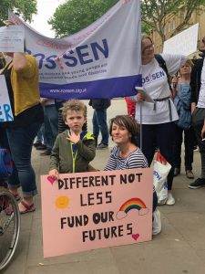 Woman and young child with placard saying "different not less, fund our futures"