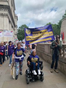 Michelle and Simone from ALLFIE holding a banner saying "We know inclusion works"
