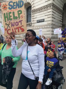 Woman in crowd with placard saying "send help not cuts"