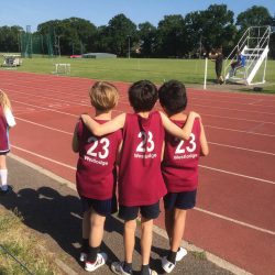 Three small boys with their arms round each other on an athletics track, backs to the camera
