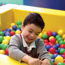 small boy in ballpit, wearing school uniform