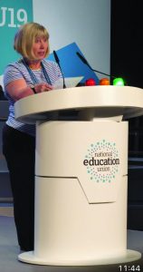 Colleen standing at a lectern delivering a speech