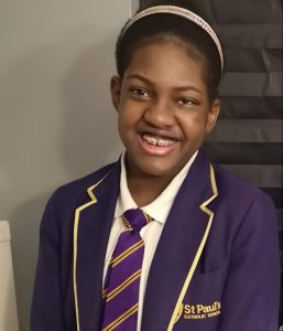 Head and shoulders shot of Kadijah Adam at school. Kadijah is a Young Black woman with her hair tied back and she is pictured in her St Paul's Catholic School uniform, which is purple and yellow.