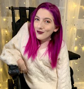 Head and shoulders shot of Melody Powell, the author of the article Online University Empowers Disabled Students. Melody is a white woman with purple hair and is pictured in a black wheelchair.