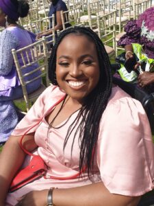 Image: Yewande Akintelu-Omoniyi, Author. Shot of Edmore, a Black woman in a pink dress, smiling at the camera.